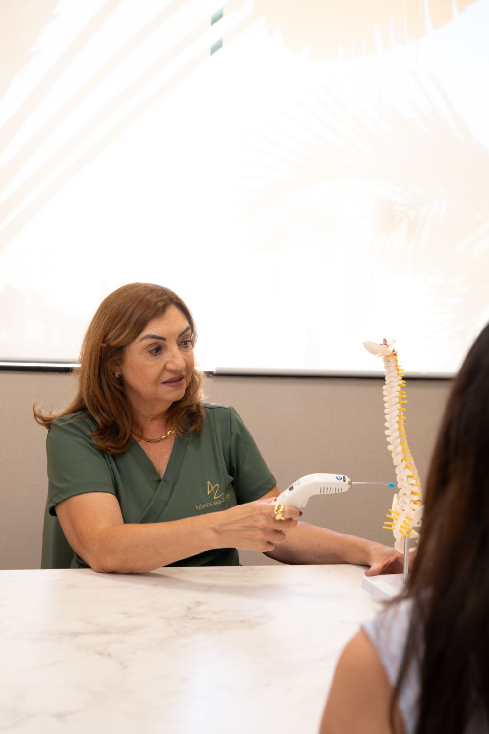 Ana Zandoná explicando a coluna vertebral com um modelo anatômico durante a avaliação