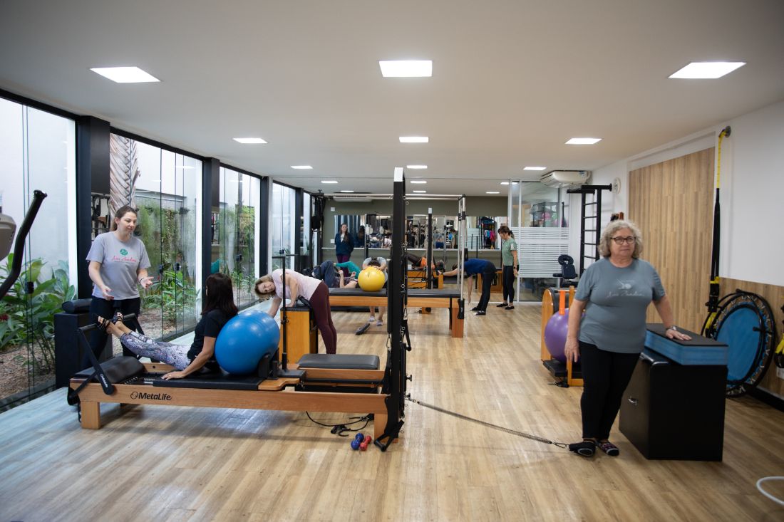 Estúdio de Pilates com aparelhos e alunos em atendimento